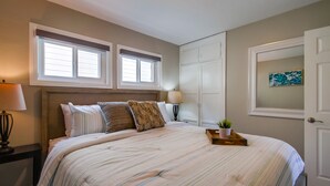 A bedroom with a bed, two windows, a nightstand, a lamp, a small plant, and a door. - Casa Azul Upper (San Diego)