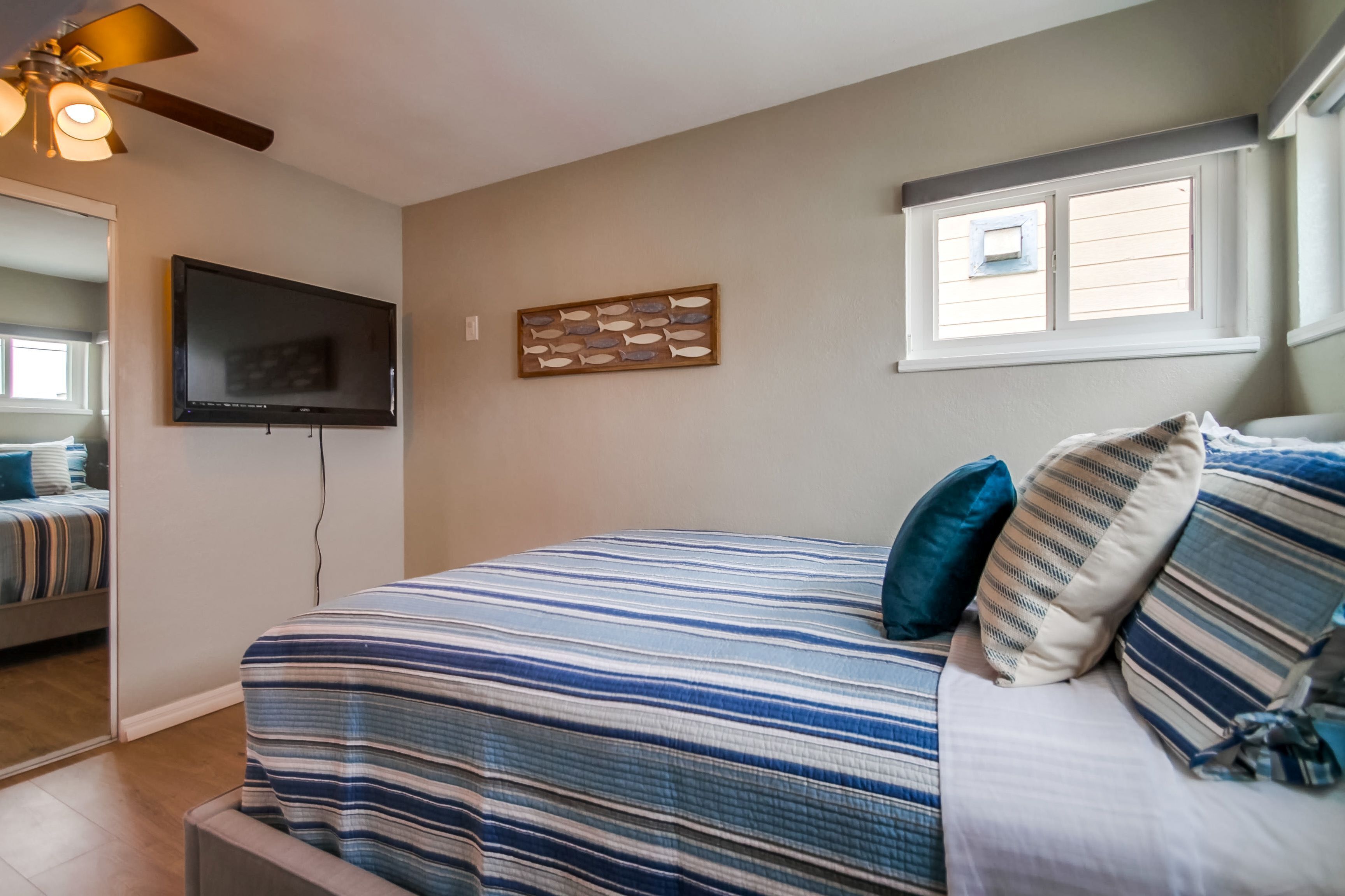 Une chambre à coucher avec un lit, un téléviseur fixé au mur, une fenêtre et un ventilateur de plafond.