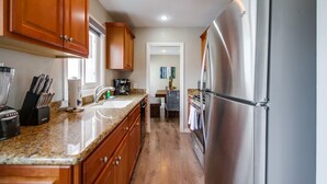 A modern kitchen with wooden cabinets, granite countertops, stainless steel appliances, and a view into the dining area. - Casa Azul Upper (San Diego)