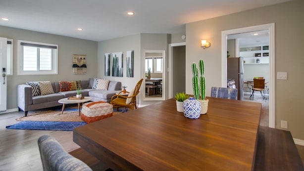A spacious living room with a wooden dining table, a gray sofa, and a coffee table. There are two chairs and a rug on the floor. - Casa Azul Upper (San Diego)