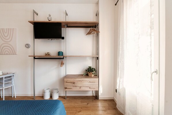 A bedroom with a bed, a desk, a chair, a wardrobe, and a window with curtains.