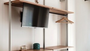 A modern interior with a mounted flat-screen TV, wooden shelves, and a hanging garment rack.