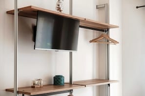 A modern interior with a mounted flat-screen TV, wooden shelves, and a hanging garment rack. - Minerva - MyHomeinComo (Como)