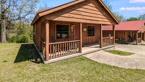 A wooden cabin with a porch, a number sign, and a red roof. - #74 Pinewood Cabin: Hog Holler (Mountain View)
