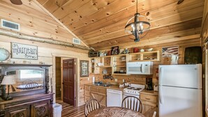 A wooden cabin interior with a dining table, chairs, a kitchen area including a stove, microwave, and refrigerator, and a sign reading "on mountain time". - #74 Pinewood Cabin: Hog Holler (Mountain View)