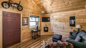 A cozy log cabin interior with a fireplace, a mounted motorcycle, a television, and a patterned sofa. - #74 Pinewood Cabin: Hog Holler (Mountain View)