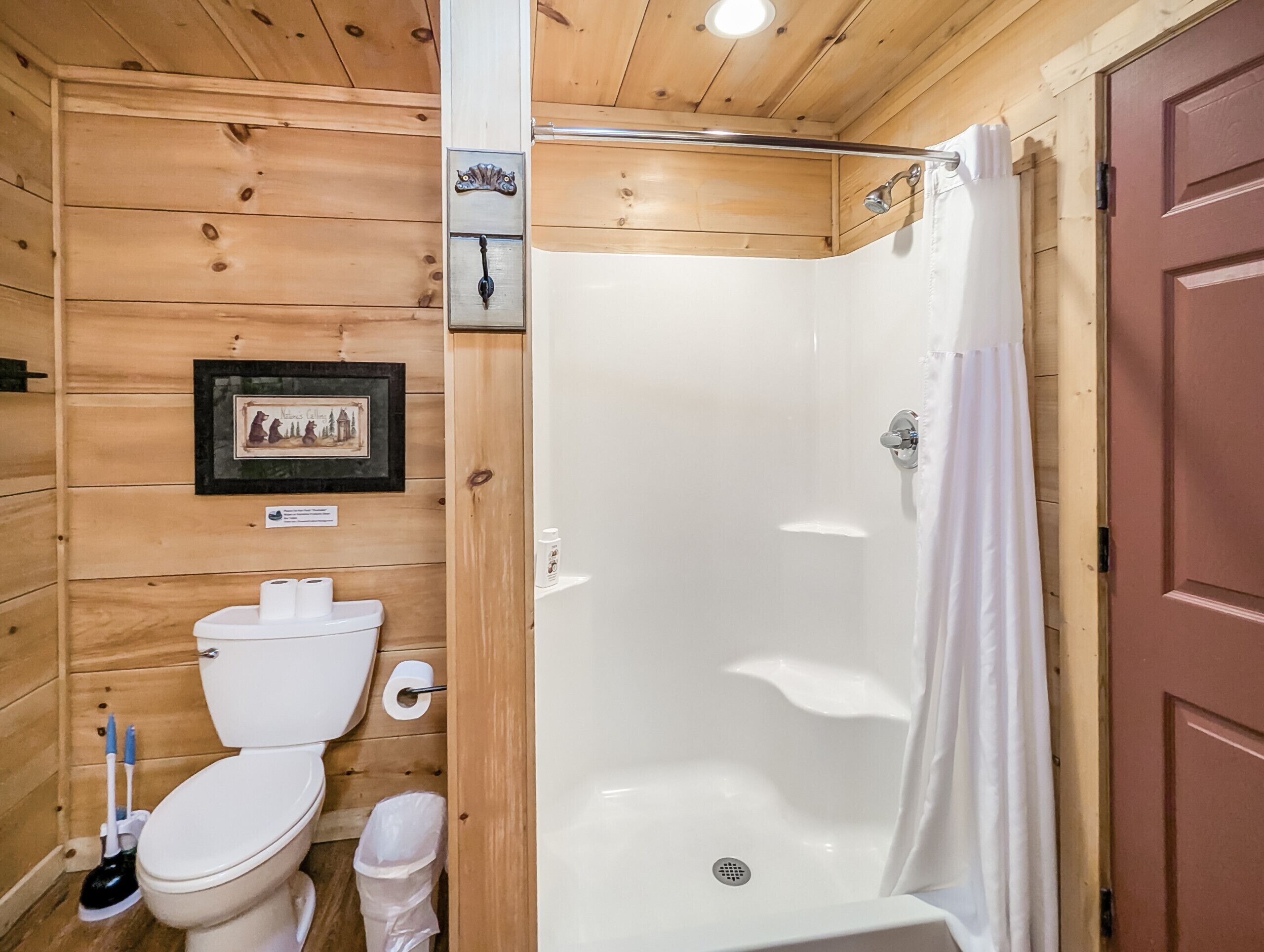 A wooden cabin bathroom with a toilet, a shower, and a door.