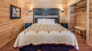 Ein Schlafzimmer einer Holzhütte mit einem Bett, Nachttischen und an der Wand befestigten Lampen.