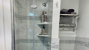 Et badeværelse med en glasafskærmet brusekabine, toilet og en hylde med toiletartikler.