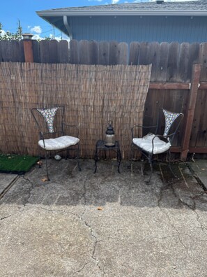 Eine Terrasse mit zwei Metallstühlen, einem kleinen Tisch und einer Laterne.