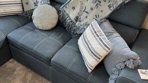 En mørk lædersofa med mange puder og plaider, placeret op ad en væg med et vindue over.