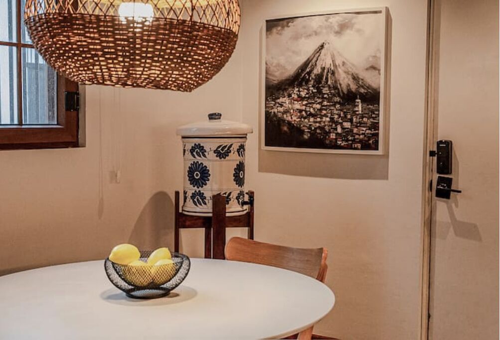 Un coin repas avec une table ronde, un saladier de fruits, une lampe décorative suspendue, un récipient en céramique de style japonais traditionnel et un tableau encadré représentant le mont Fuji.