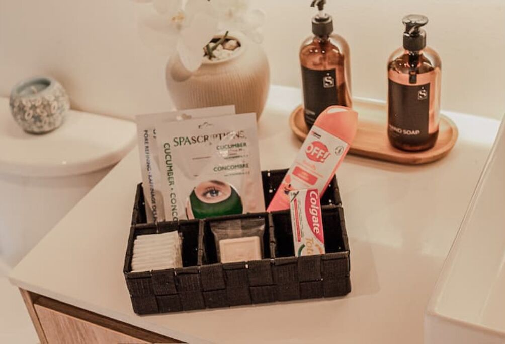 Un meuble-lavabo de salle de bain avec un distributeur de savon noir, un flacon de savon pour les mains, un tube de dentifrice Colgate, un flacon de bain de bouche Spascriptions et un petit vase avec une fleur.
