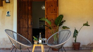 Une porte en bois, deux chaises en osier, une petite table avec une bouteille et des verres, et des plantes en pot.