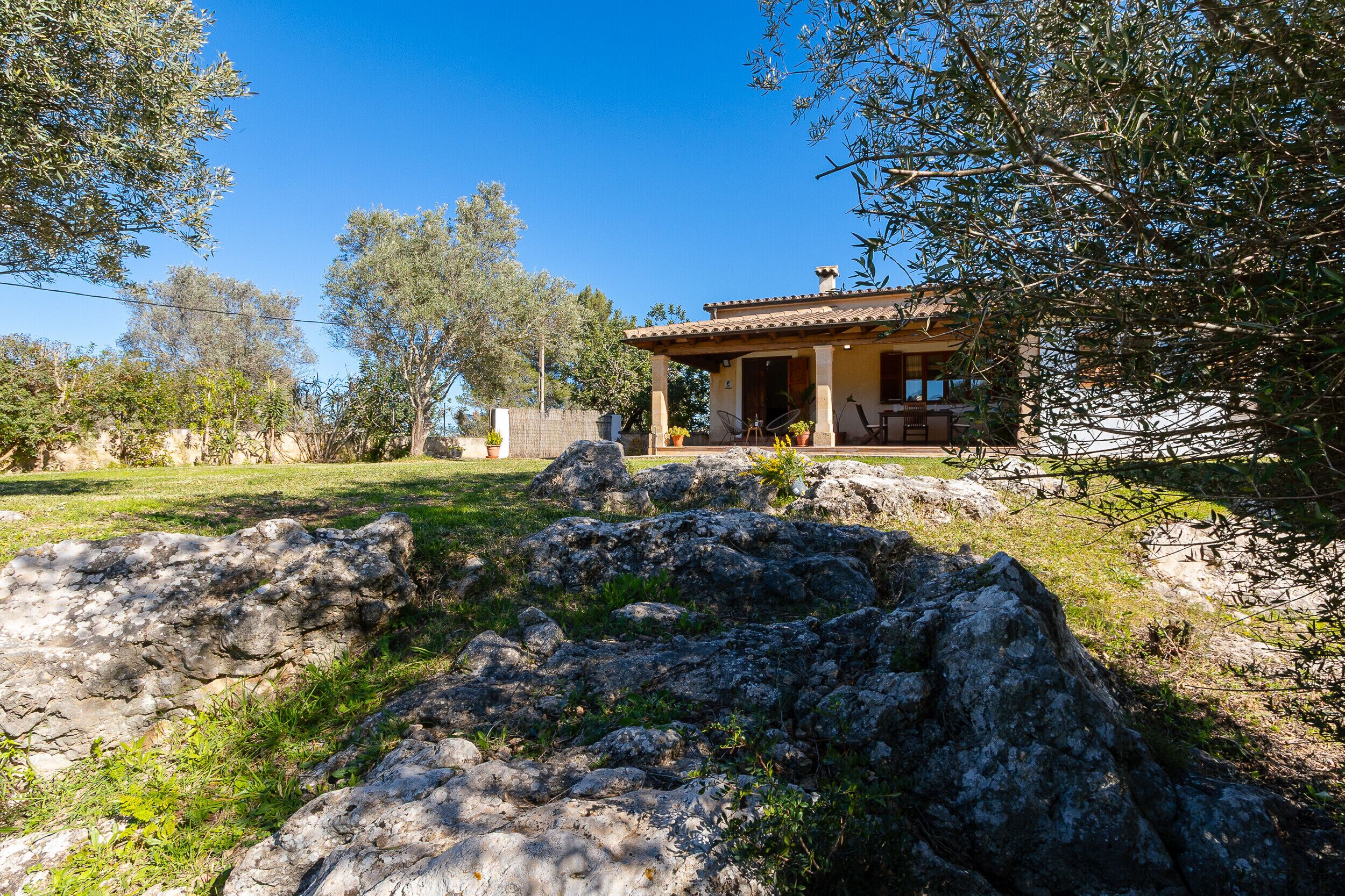 A rustic house with a tiled roof, surrounded by a grassy area and large rocks.