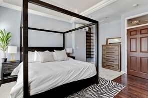 A four-poster bed with a dark frame, white bedding, and a zebra-patterned rug.