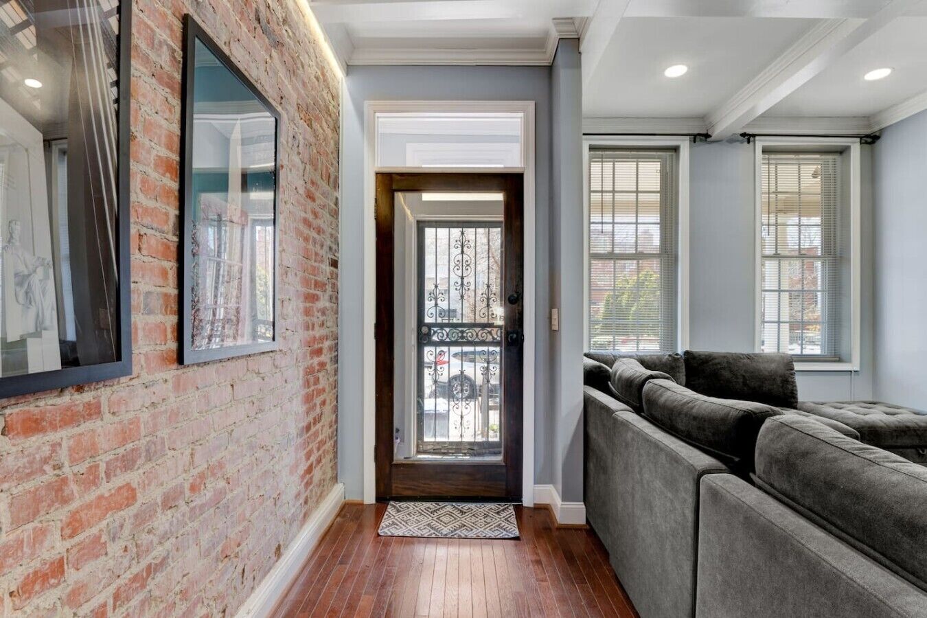A hallway with a brick wall, a door with a metal gate, and a grey sofa.