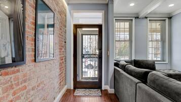 A hallway with a brick wall, a door with a metal gate, and a grey sofa.