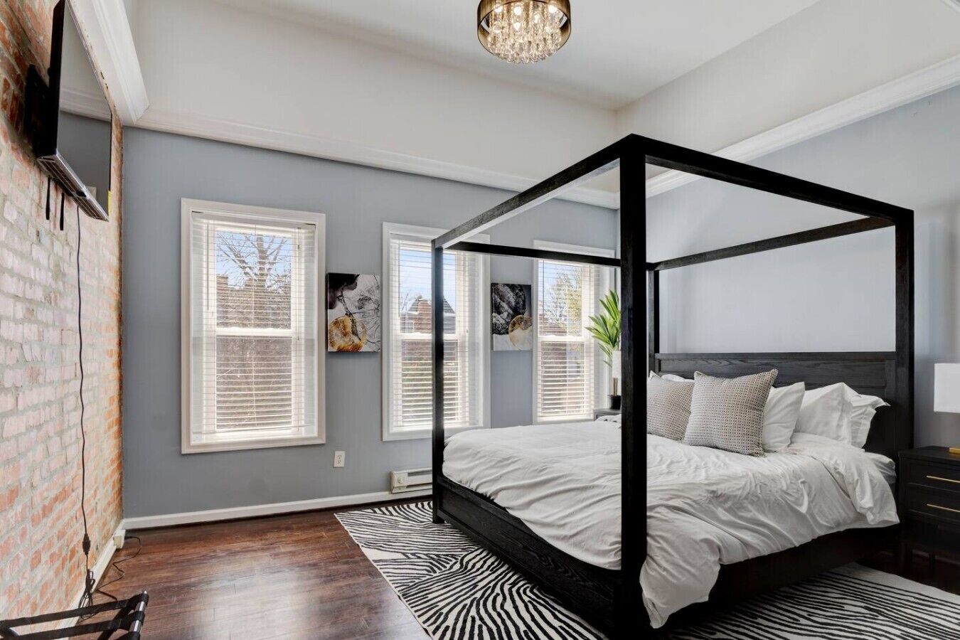 A four-poster bed in a bedroom with a zebra-patterned rug, a chandelier, and artwork on the walls.