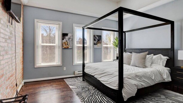A four-poster bed in a bedroom with a zebra-patterned rug, a chandelier, and artwork on the walls.