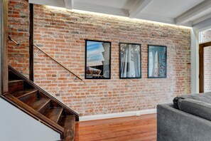 A staircase leading to a living area with a brick wall and three framed artworks. - Phoenix`s Place Cap Hill | King Bed | Walk to H St (Washington)