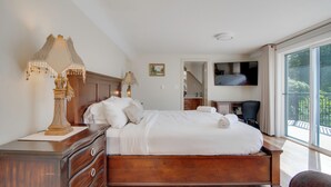 A spacious bedroom with a large bed, wooden headboard, bedside lamps, and a view of the outdoors through a large window. - Oceanfront Getaway with Private Dock + Beach (Sooke)