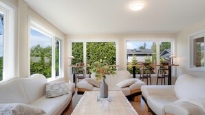 A spacious living room with a large window, a sofa, a coffee table, and a dining area with chairs and a table. - Oceanfront Getaway with Private Dock + Beach (Sooke)