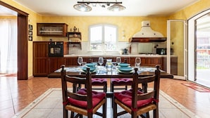 Zona pranzo con tavolo apparecchiato per quattro persone, cucina con piano cottura e forno, e un'ampia finestra.
