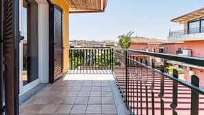 Un balcone con pavimento piastrellato, ringhiera in metallo e vista sui palazzi circostanti.