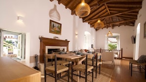 A dining area with a wooden table, woven chairs, and a fireplace. - Elegant Hydra Getaway (Idra)