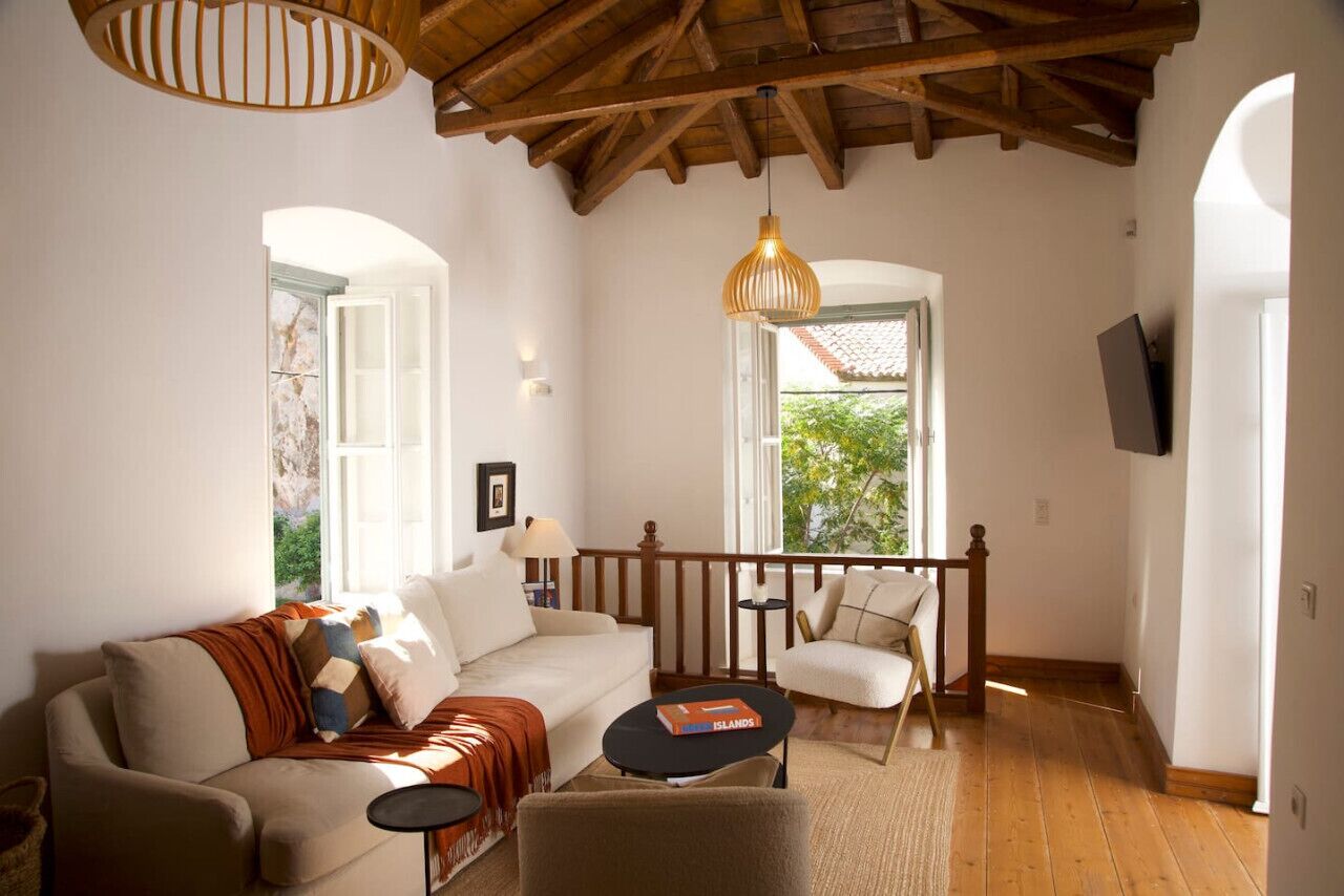 A cozy living room with a wooden ceiling, a sofa, a chair, a small table, and a bookshelf.