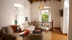 A cozy living room with a wooden ceiling, a sofa, a chair, a small table, and a bookshelf. - Elegant Hydra Getaway (Idra)
