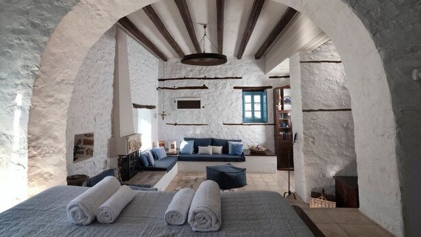A rustic room with a stone wall, wooden beams, a sofa, and a bed with rolled towels. - Historical Stone Manor-Upper Floor (Idra)