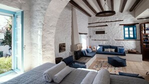 A cozy room with a stone wall, a wooden ceiling, a blue sofa, and a bed with rolled towels. - Historical Stone Manor-Upper Floor (Idra)