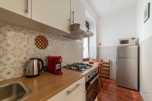 A kitchen with a stove, coffee maker, kettle, microwave, and refrigerator.