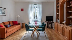 Een woonkamer met een bank, een glazen tafel met stoelen, een televisie en een boekenkast.