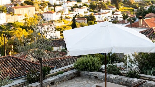 A rooftop terrace with stone flooring, lounge chairs, and a white umbrella. - Villa Alethea Retreat (Idra)