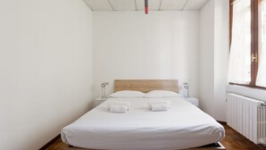 Een enkel bed met witte lakens, een houten hoofdbord, nachtkastjes met lampen en een raam met gordijnen.
