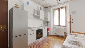 Een compacte keuken met een koelkast, oven en spoelbak, een eettafel met een tafelkleed met patroon, en een raam met gordijnen.