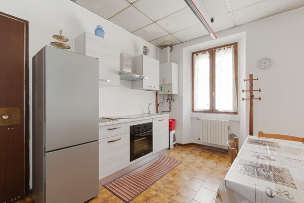 Una cocina compacta con refrigerador, horno y lavamanos, una mesa de comedor con mantel estampado y una ventana con cortinas.