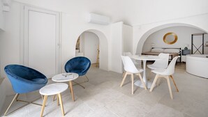 Ein modernes Interieur mit Essbereich, zwei blauen Stühlen, einem weißen Tisch und einem Bett mit weißem Kopfteil.