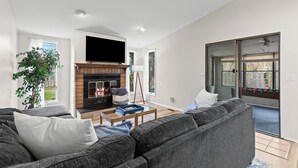 Un salon moderne avec une cheminée, des canapés gris, un téléviseur à écran plat et une grande fenêtre.