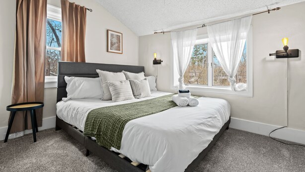 Une chambre à coucher avec un lit, une fenêtre avec des rideaux, une table de chevet et une lampe fixée au mur.
