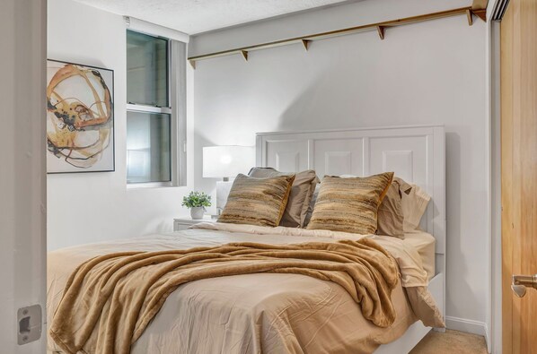 Une chambre à coucher avec un lit, une table de chevet, une lampe et une fenêtre.