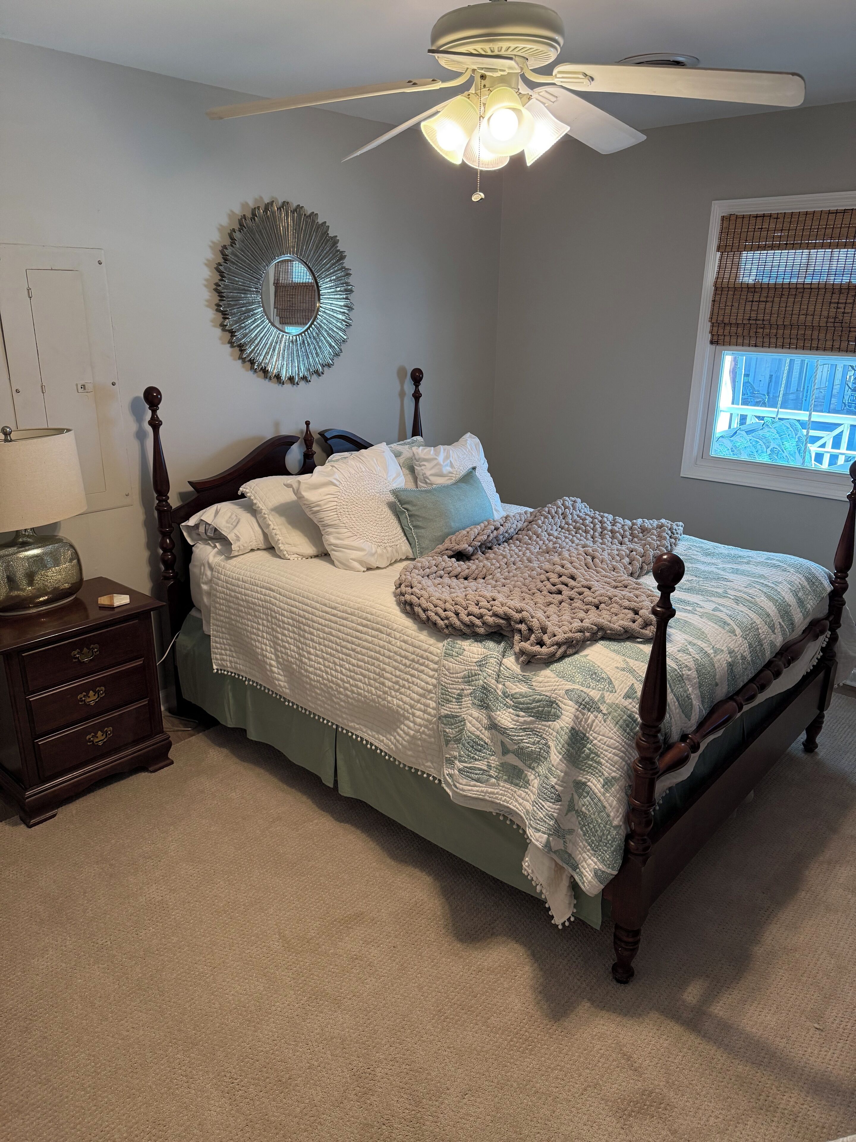 A neatly arranged bedroom with a bed, a nightstand, a mirror, and a ceiling fan.