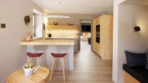 A modern kitchen with a central island, wooden flooring, and a dining area with stools. - Villa Cavazzal - Exclusive apartment (Cavalese)