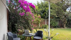 Un patio exterior con dos sillas y una mesa, rodeado de abundante follaje y plantas florecientes.