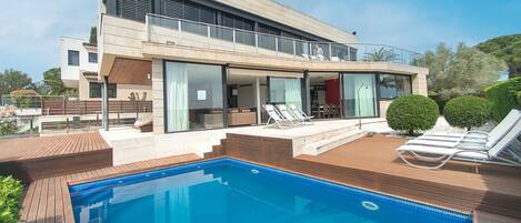 A modern house with a swimming pool, a balcony, and a deck with lounge chairs.
