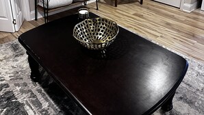 Un salon avec une table basse en bois foncé, un téléviseur posé sur un meuble en bois, une porte blanche et un mur blanc sur lequel est installé un climatiseur.