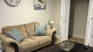 Un salon avec un canapé beige, deux coussins à motifs, une horloge ronde, un globe terrestre et une table basse en bois foncé.